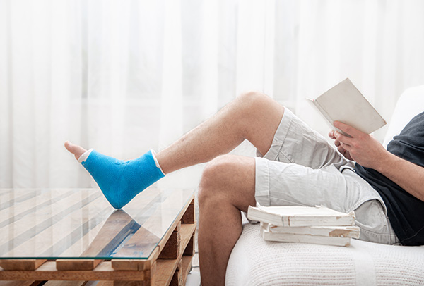 Man on sofa with leg in cast up on a table reading books