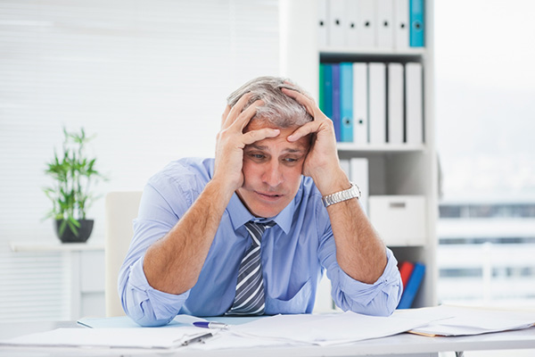Man sat at desk full of paperwork with head in his hands