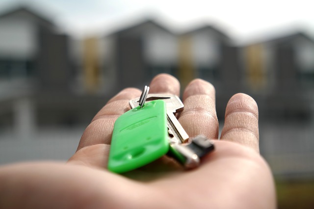 Hand holding house key with homes in the background