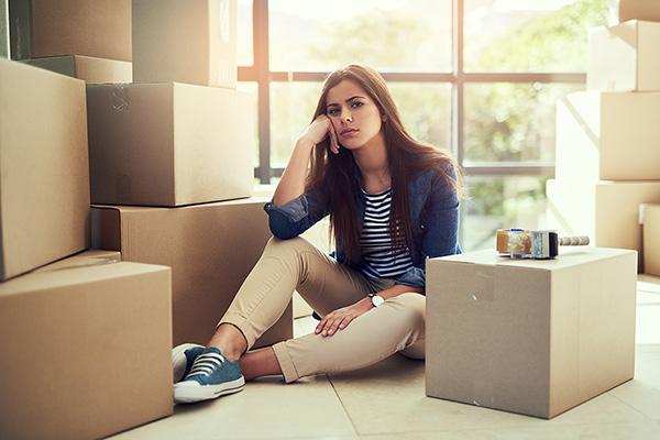 Woman sitting amongst moving boxes looking disappointed
